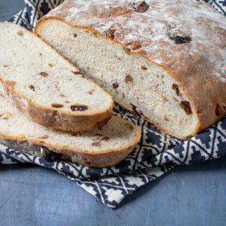 A freshly baked date and walnut loaf on a blue background with patterned tea towel and two slices cut from the bread.