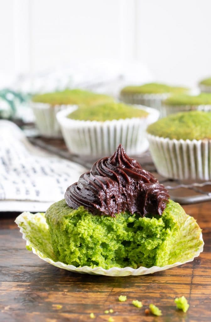 A bright green Cavolo Nero kale cupcake with a bite taken out, topped with chocolate frosting