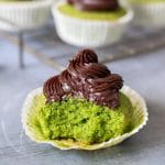 A green (kale) Cavolo Nero cupcake with chocolate frosting. A bite has been taken out and others are on a cooling rack in the background.