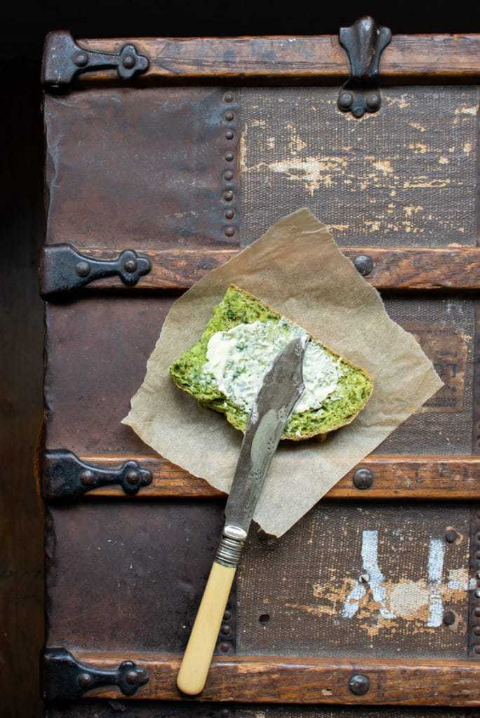 A slice of bright green kale herb soda bread with butter and vintage knife on antique trunk. An easy no-rise bread recipe