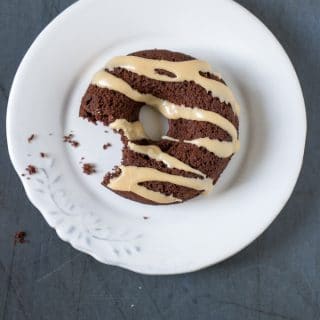 Overhead photo of a vegan chocolate donut with Earl Grey drizzle on a white plate with a bite taken out.