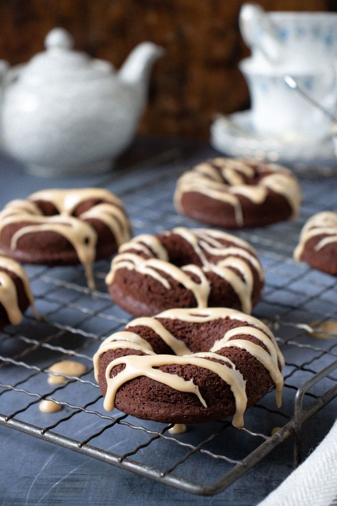 Vegan chocolate doughnuts with Earl Grey drizzle on a vintage cooling rack with teacups and teapot in the background