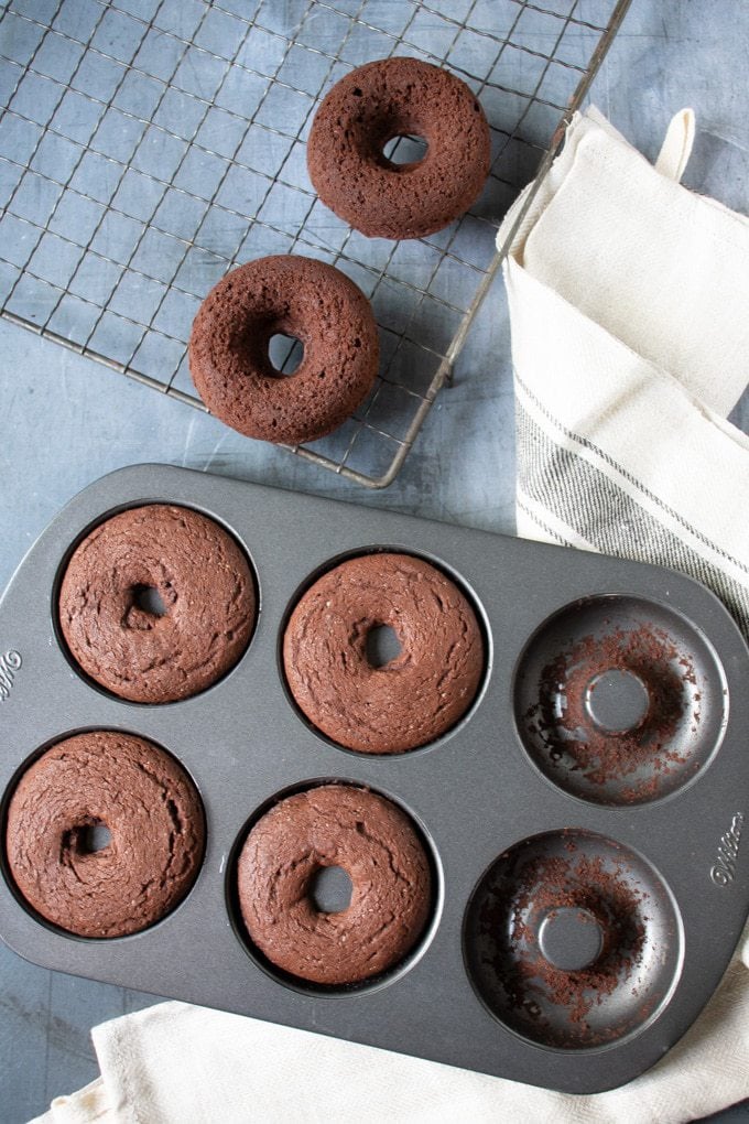 A tray of baked chocolate vegan donuts next to a vintage cooling rack.