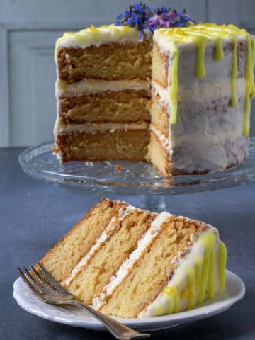 A vegan lemon layer cake that's light and fluffy with lemon icing and bright yellow lemon drizzle icing, with a slice cut out