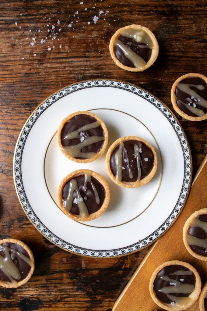 Close up of three mini chocolate tarts with salted caramel drizzle on a white plate. Get the recipe. 