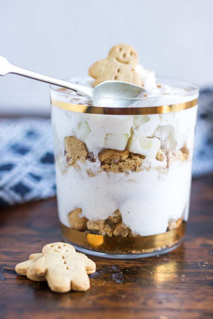 A glass of no bake layered dessert: Pear Gingerbread Parfaits - layers of crushed gingerbread men, gingerbread spiced yogurt and chopped pear. 