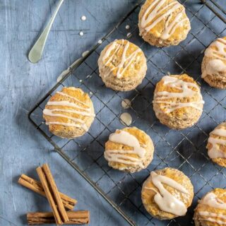 A vintage rack with cinnamon scones with vanilla cinnamon drizzle, next to a spoon and cinnamon sticks. Get the recipe.