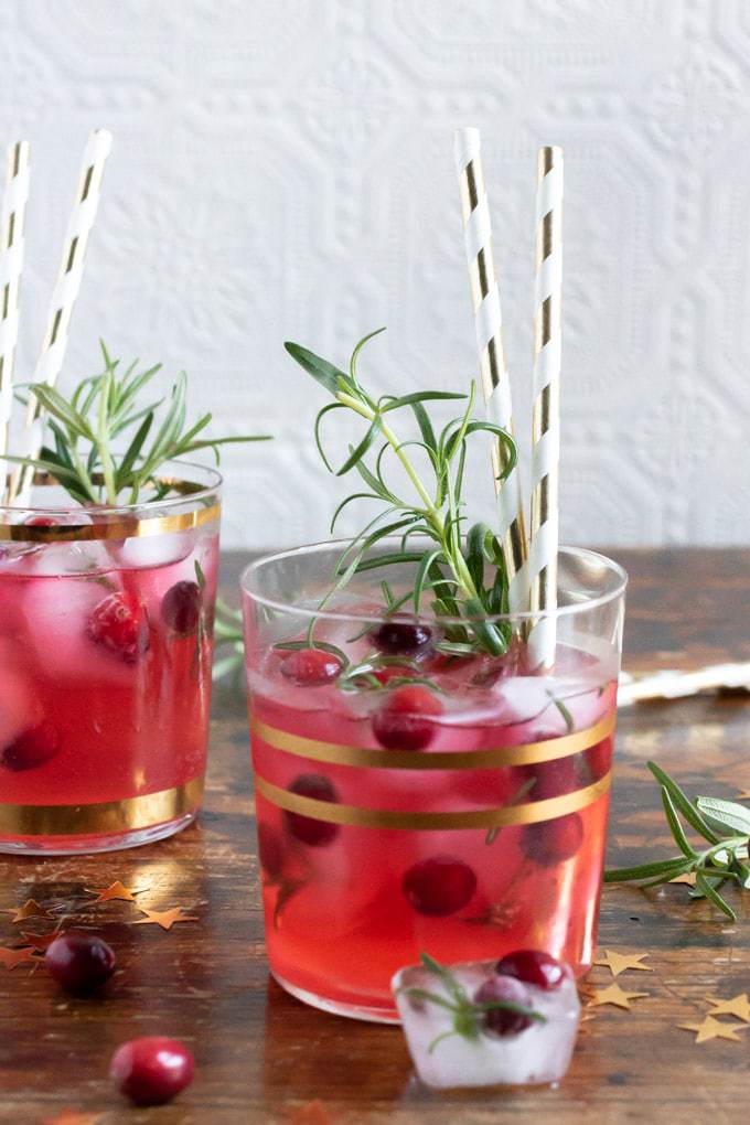 Glasses of ginger cranberry kombucha cocktail recipe with gold paper straws and sprigs of rosemary