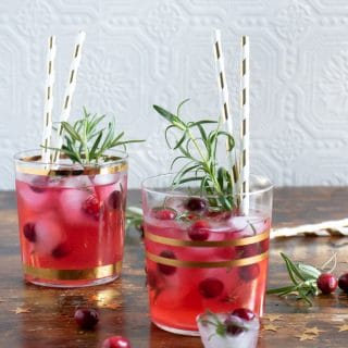 Glasses of ginger cranberry kombucha cocktail recipe with gold paper straws and sprigs of rosemary