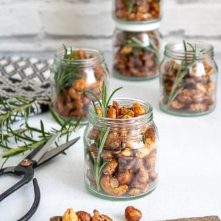 Small jars of Rosemary Maple Spiced Roasted Nuts with sprigs of rosemary, next to vintage scissors