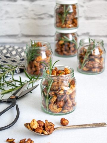 Small jars of Rosemary Maple Spiced Roasted Nuts with sprigs of rosemary, next to vintage scissors