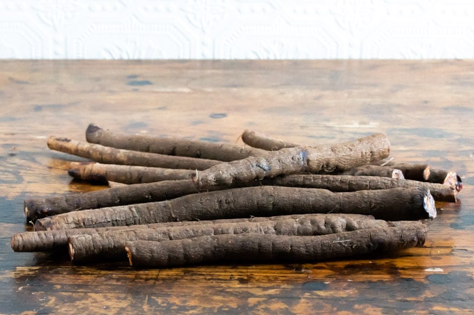 A pile of Salsify - a root vegetable - on a wooden table with a white textured wall in the background