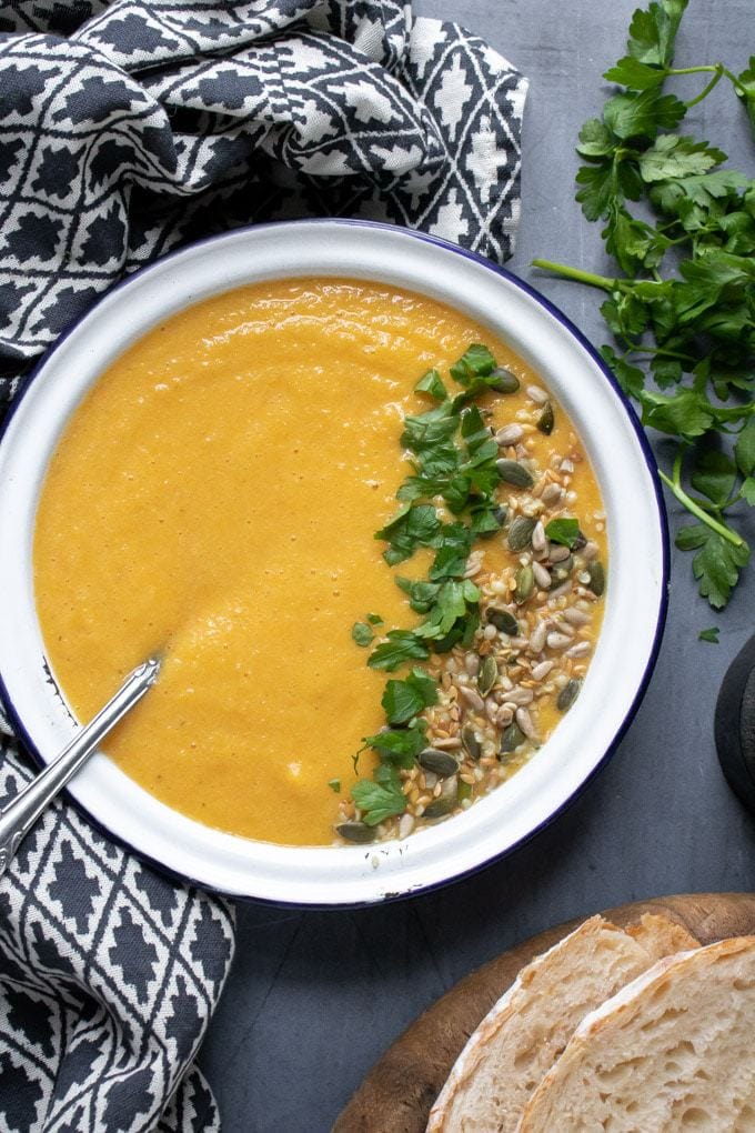 A bowl of creamy vegan lentil soup, topped with fresh herbs and seeds. On a blue background with fresh herbs scattered around.
