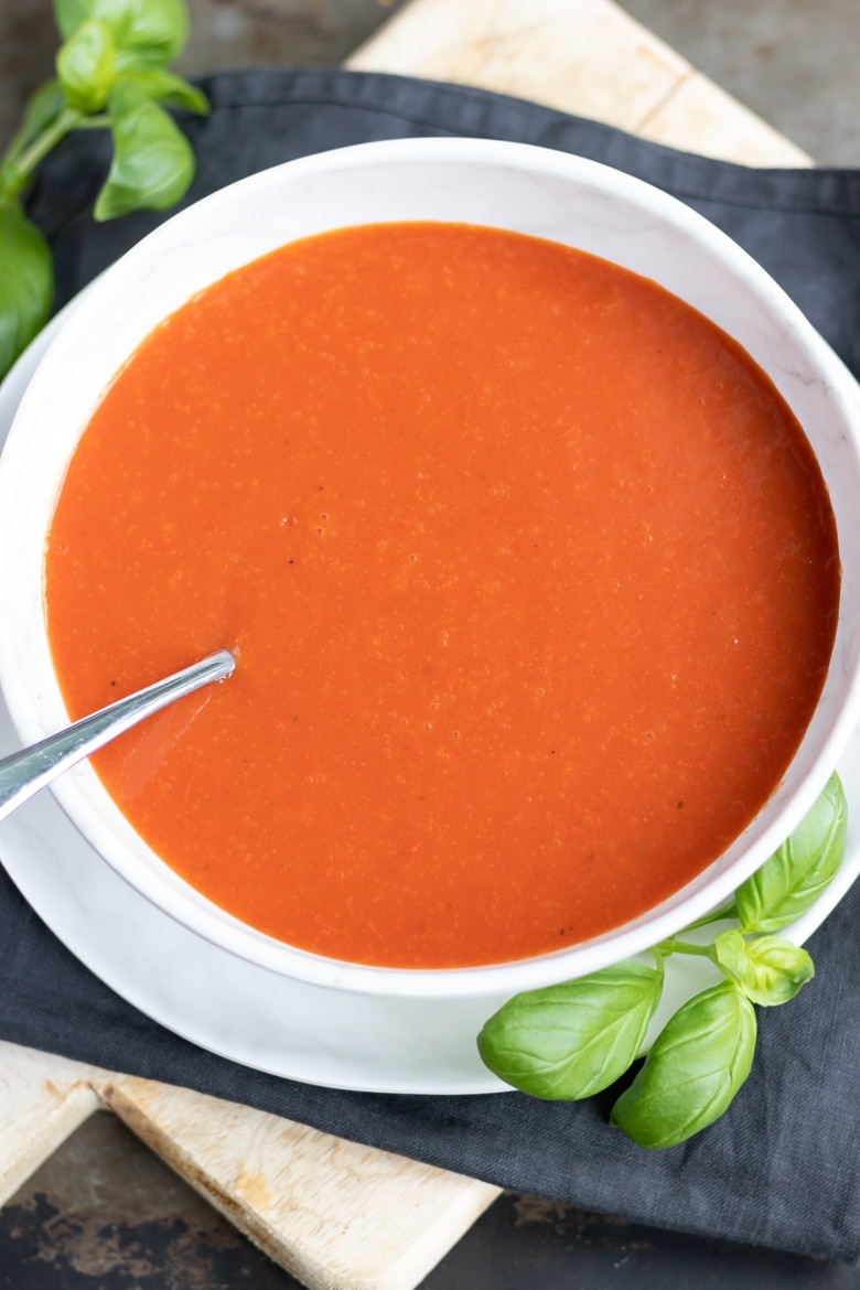 Close up of a bowl of homemade tomato soup using canned or fresh tomatoes. Next to fresh basil leaves.