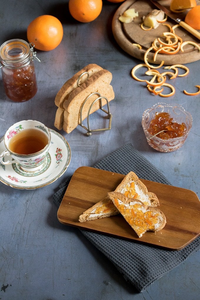 A bowl and jar of ginger orange marmalade (an easy recipe) next to marmalade on toast and teacups.