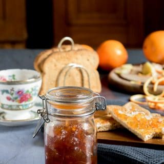 A jar of homemade ginger orange marmalade preserves recipe, in front of toast and teacups.