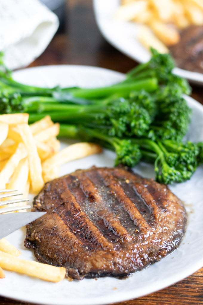 Close up of a mushroom steak on a plate with broccoli and fries.