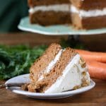 A slice of two layer vegan carrot cake. It's moist, fluffy and delicious one bowl easy recipe. Shown with vegan cream cheese frosting and walnuts.