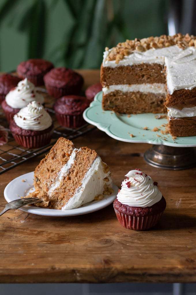 A vegan carrot cake with vegan cream cheese frosting and vegan red velvet cupcakes with thick swirls of vegan cream cheese frosting.
