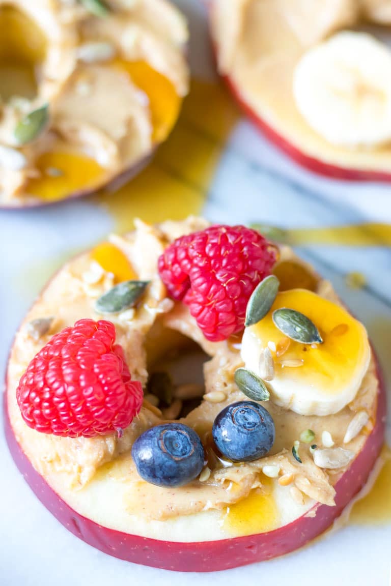 Close up of an apple ring topped with peanut butter, fruit and seeds.