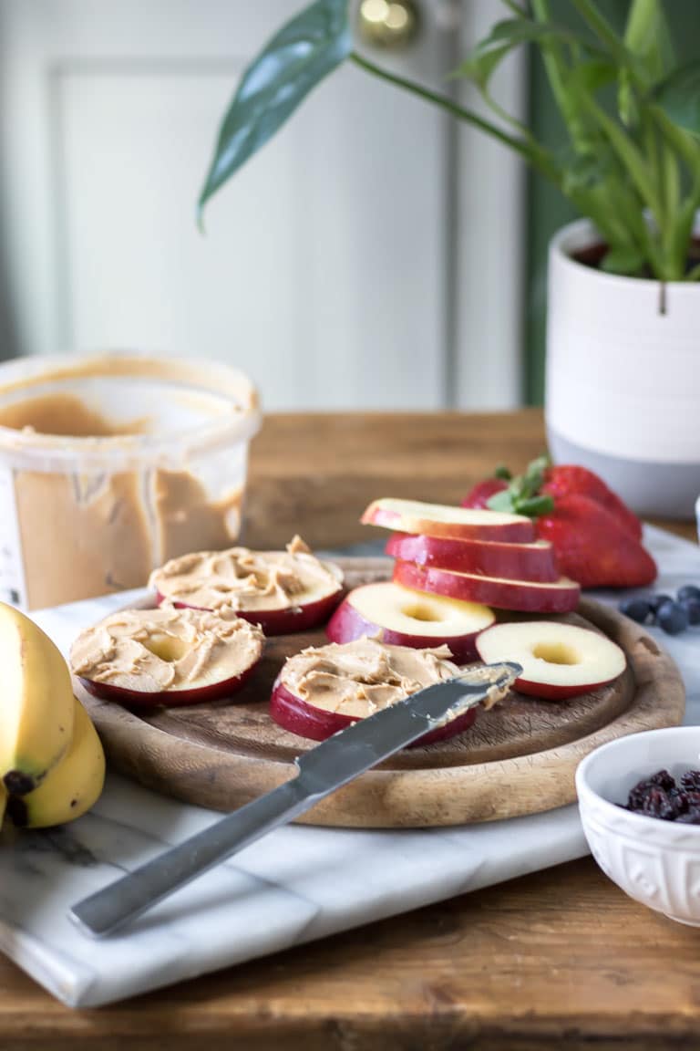 Apple pizzas - healthy snack ideas. A chopping board with slices of apple being spread with peanut butter. Get the easy recipe now. 