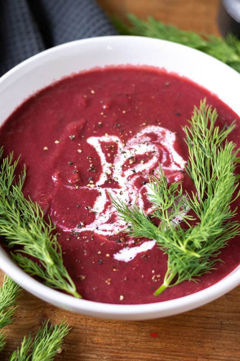 Close up bowl of beet soup with dill sprigs.