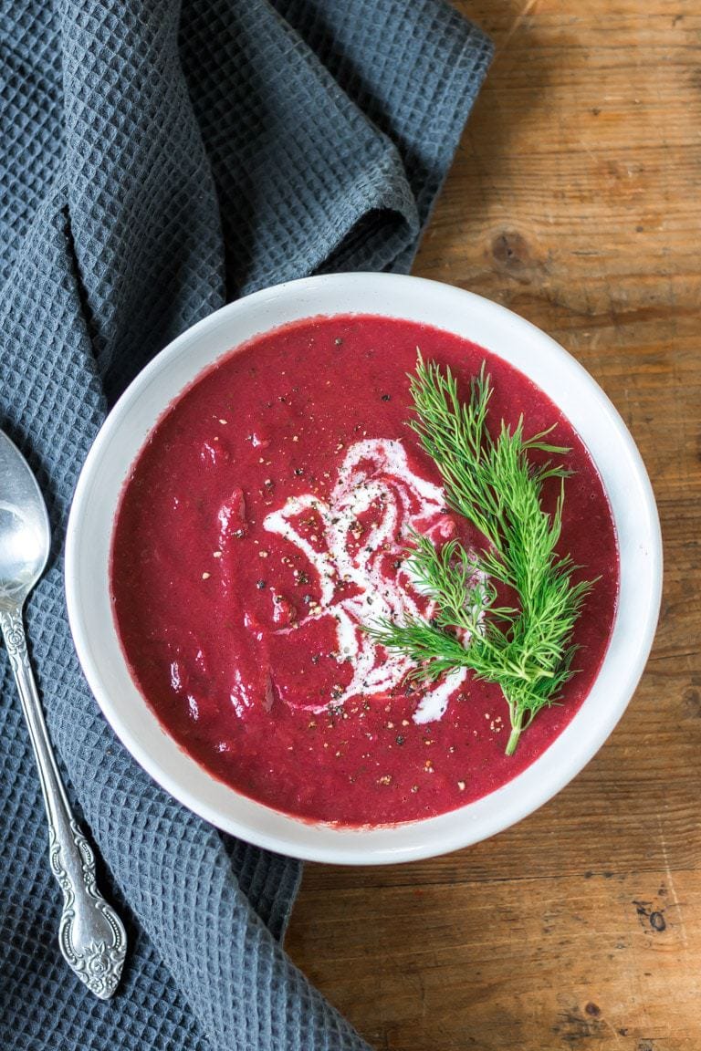 Bowl of beetroot soup with cream and dill sprigs.