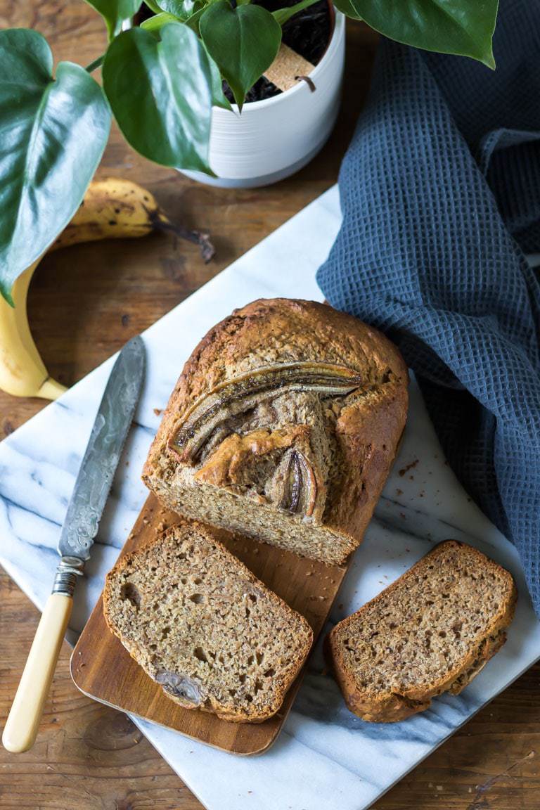 Moist and easy one bowl vegan banana bread with slices cut out next to a banana and plant. Get the recipe. 