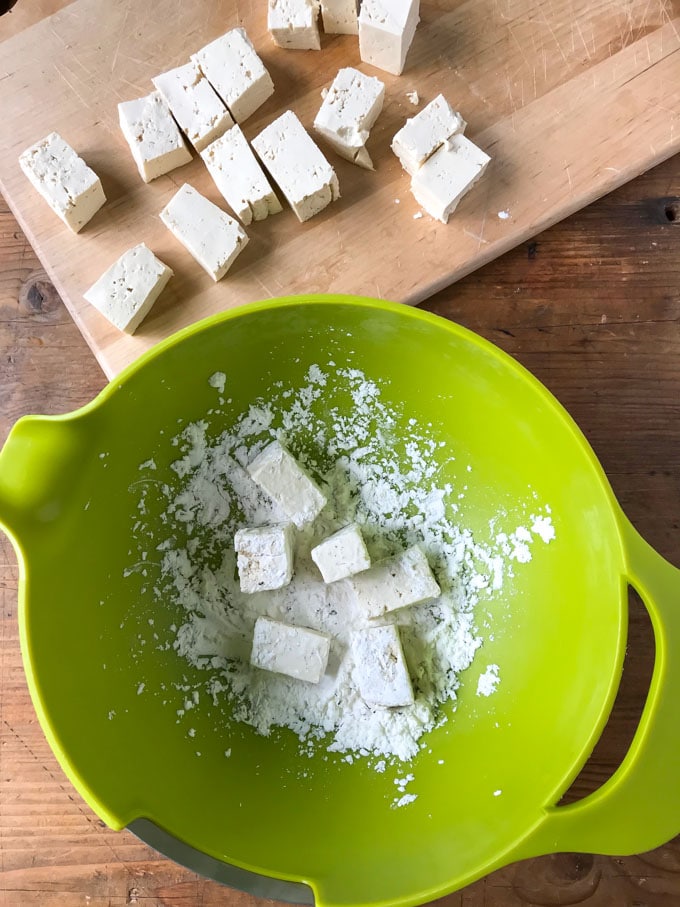 Cutting tofu and coating it in cornstarch.