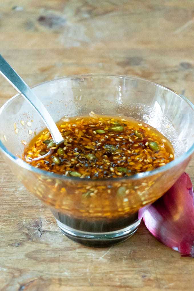 A bowl of vegan salad dressing with toasted seeds, balsamic vinegar, maple syrup and paprika.