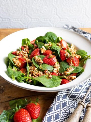 A bowl of colorful tasty strawberry spinach salad with walnuts and a 5 ingredient toasted seed dressing with balsamic and maple syrup. Vegan recipe.