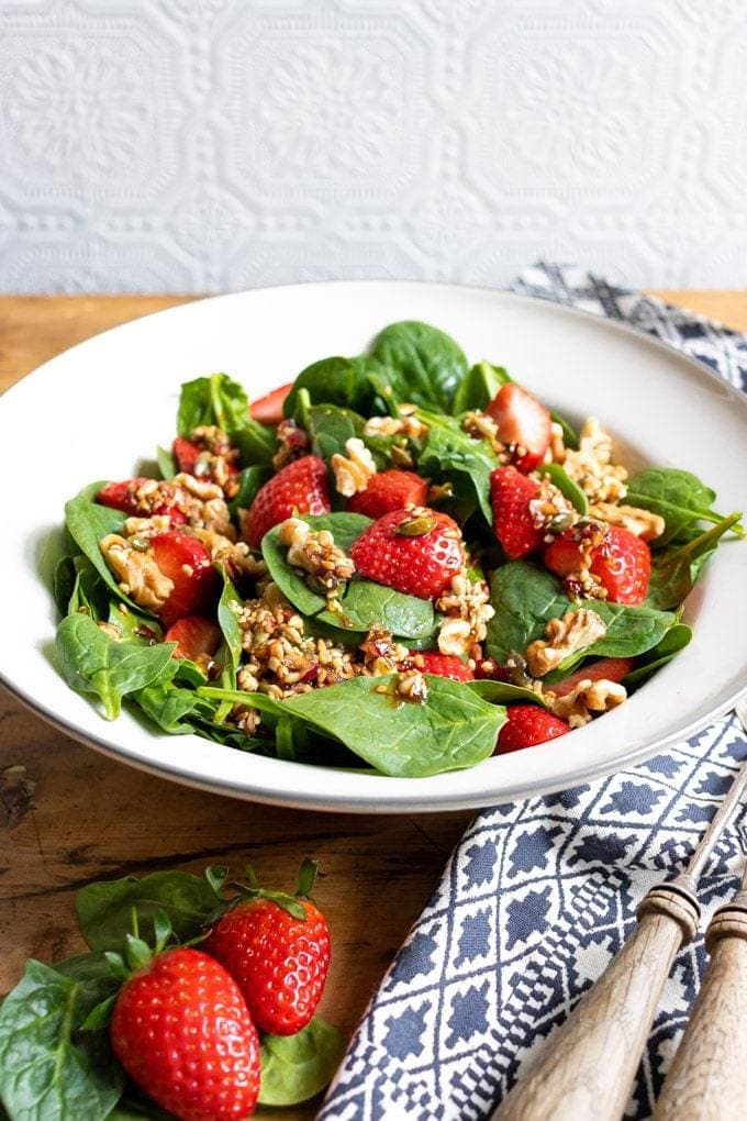 A bowl of colorful tasty strawberry spinach salad with walnuts and a 5 ingredient toasted seed dressing with balsamic and maple syrup. Vegan recipe. 