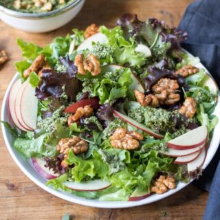 Table with a salad full of walnuts, apples and lettuce.