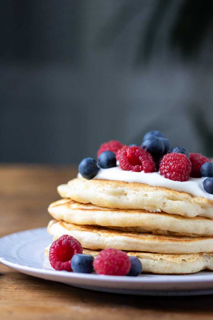 Close up of piled pancakes topped with berries.