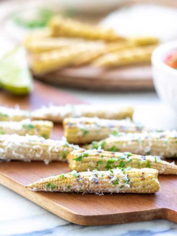 Close up of a mini elote Mexican Street corn made with baby corn. Shown sprinkled with parmesan and herbs.