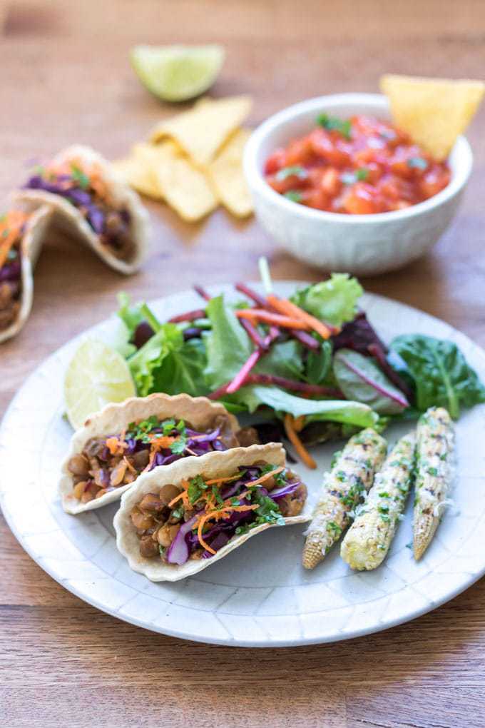 Mini taco shells with lentil taco filling on a plate with mini mexican corn