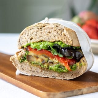 Close up of a cut roasted vegetable sandwich with pea pesto on a wooden board.