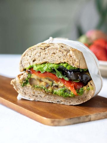 Close up of a cut roasted vegetable sandwich with pea pesto on a wooden board.