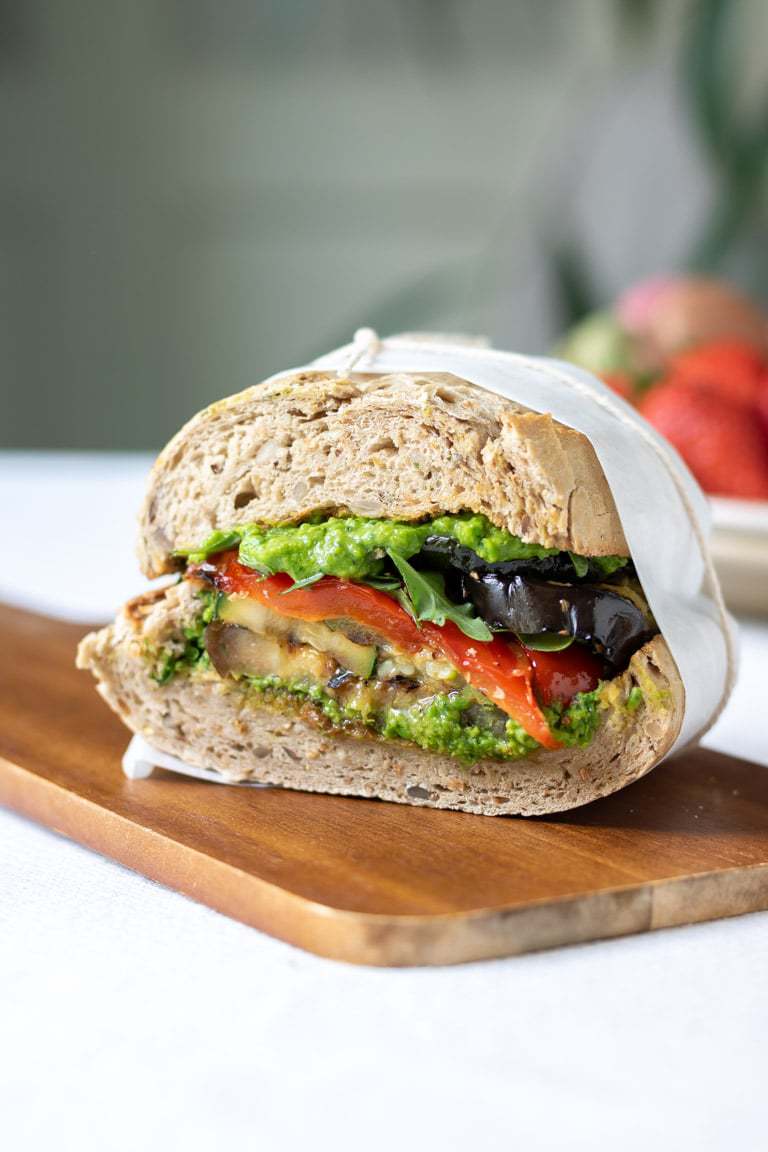 Close up of a cut roasted vegetable sandwich with pea pesto on a wooden board.