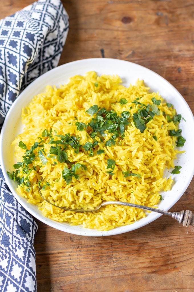 A serving bowl of yellow rice topped with fresh herbs.