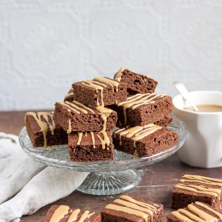 A vintage glass cake stand with Barleycup brownies piled onto it with a few brownies scattered around.