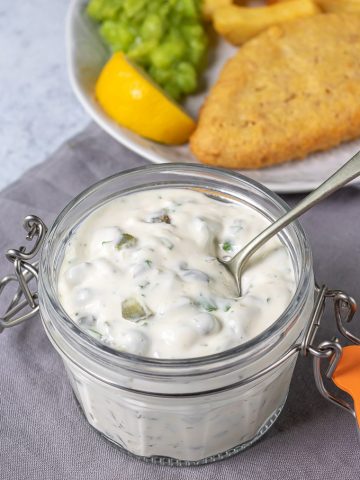 A jar of homemade tartar sauce in front of a plate of fish n chips