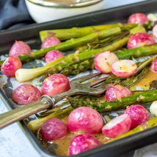 A roasted vegetable sheet pan meal with roasted radishes and asparagus with a bowl of maple mustard dressing.