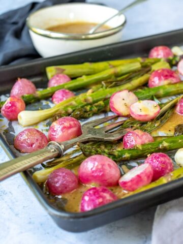 A roasted vegetable sheet pan meal with roasted radishes and asparagus with a bowl of maple mustard dressing.