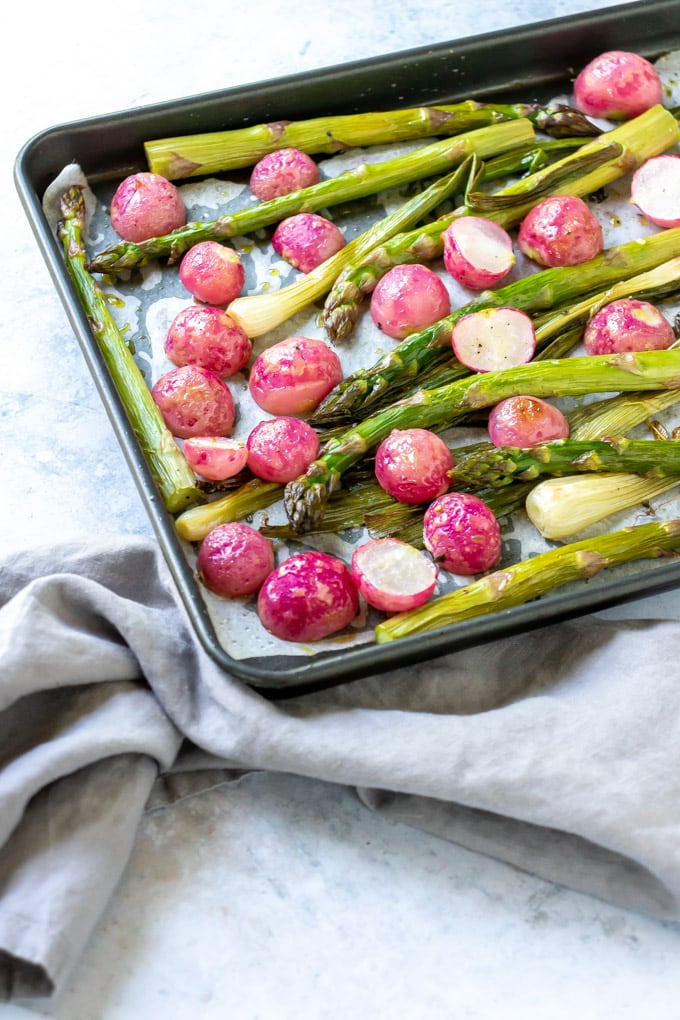 The corner of a sheet pan roasted vegetable tray with radishes and asparagus