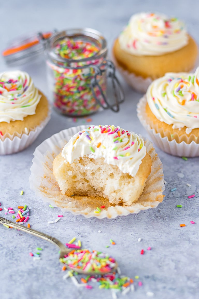 A vegan cupcake with a bite taken out. Covered in vanilla frosting and sprinkles.