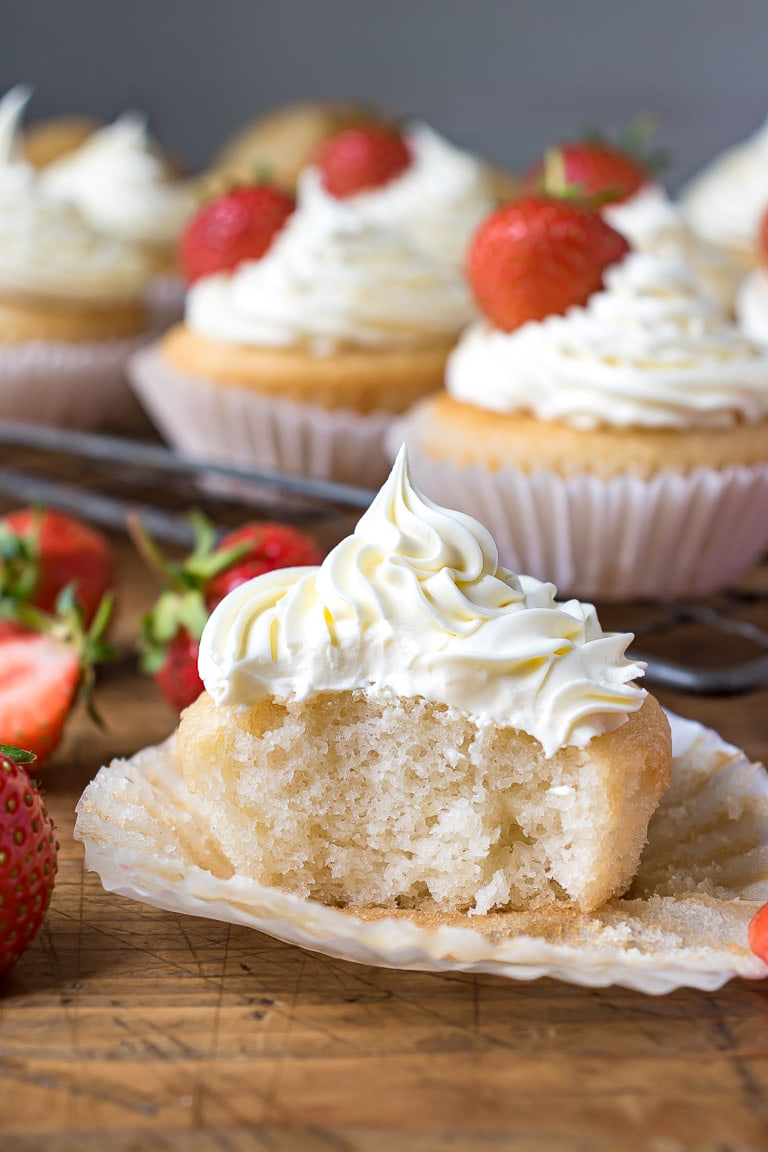 Vegan vanilla cupcake with a bite out, with vegan frosting and strawberries.
