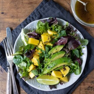 mango salad with lettuce and avocado and lime ginger dressing on a plate on a napkin