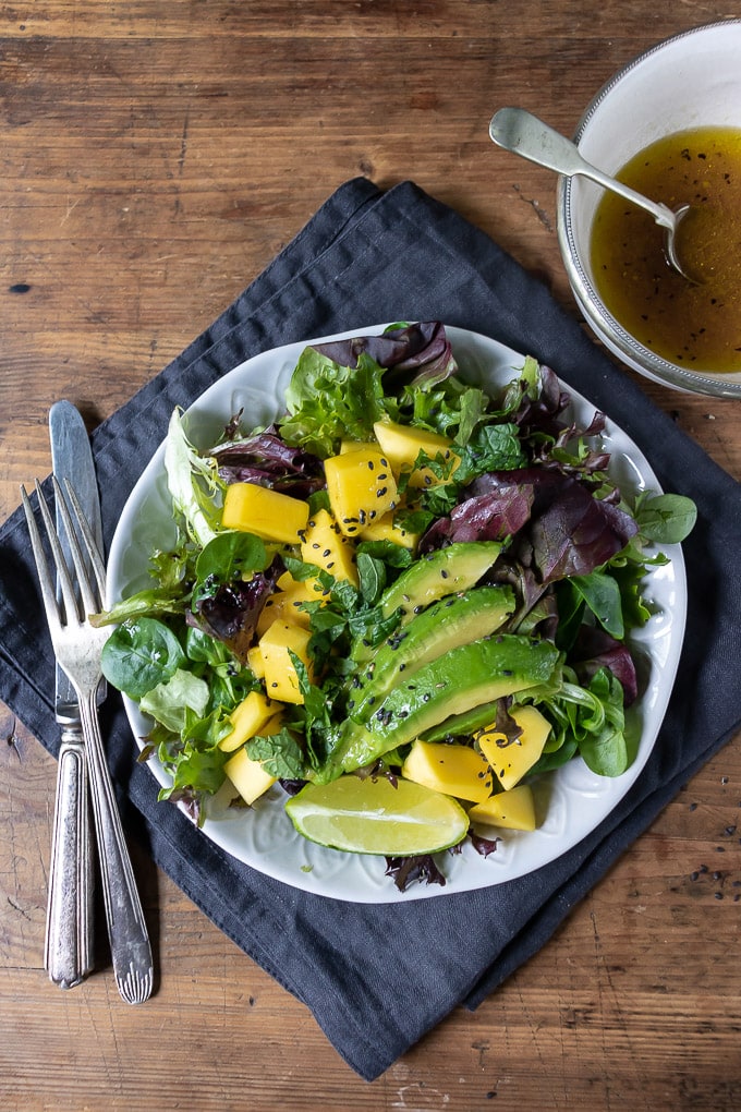 mango salad with lettuce and avocado and lime ginger dressing on a plate on a napkin