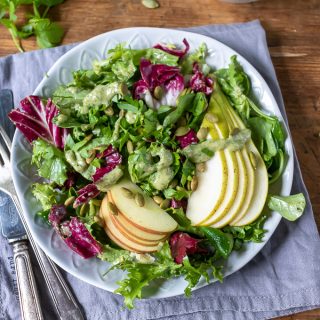 A plate of leafy green salad with radicchio, topped with apples, pears and pumpkin seed dressing